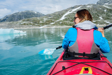 Obraz premium Woman kayaking on Styggvatnet glacier lake near Jostedalsbreen glacier.