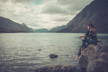 Beautiful woman posing on the shore of a wild lake, with mountains on the background.