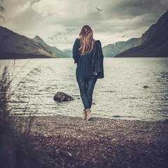 Beautiful woman posing on the shore of a wild lake, with mountains on the background.