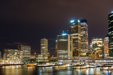 Obraz na płótnie Canvas Circular Quay railway, train station and ferry wharfs with Sydney Central Business District cityscape skyscrapers at the background. Night shot, long exposure, copy space