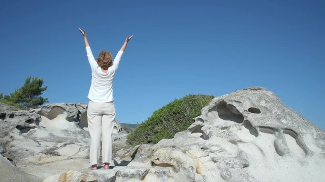 Woman with hands up standing on the hill near the sea