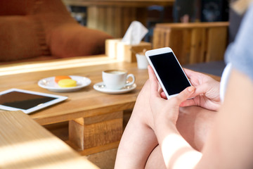 Young woman read something on her smart phone while sitting in modern cafe with tablet, cup of coffee, macarons and tablet on the table. Close up of girl hands.