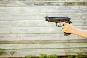 Child's hand with a gun, isolated on old wall background, outdoors closeup