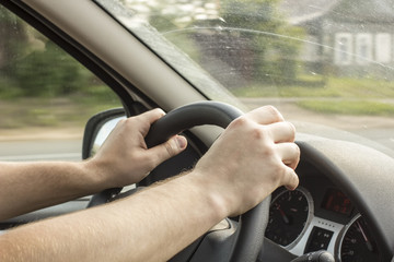 Inside view of how a man is driving a car behind the wheel and riding to the countryside, a village house in the background