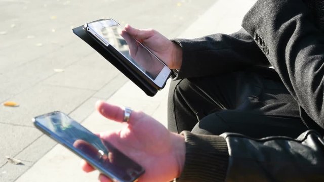 Close up on the hands of two young man holding smart phone and tablet, tapping and scrolling touchscreen &ndash; technology, social network, communication concept