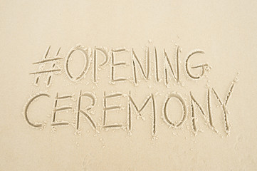 Simple hashtag Opening Ceremony message handwritten on smooth sand beach