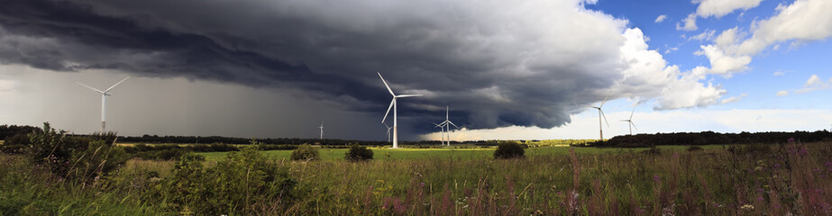 Panorama of windmills on rural field in the storm clouds and rain. Wind turbines panorama in...