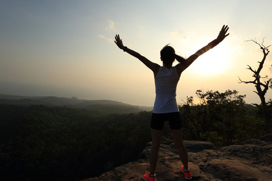 silhouette of young successful woman open arms on sunset mountain peak