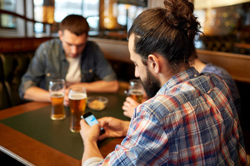 close up of men with smartphones and beer at bar