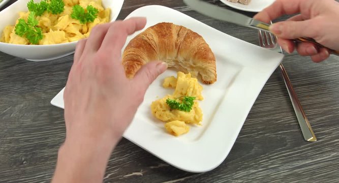 4K Clip eines Fr&uuml;hst&uuml;ckes. Ein H&ouml;rnchen und etwas R&uuml;hrei liegen auf einem eckigen weissen Teller. Eine Frau schneidet das H&ouml;rnchen.