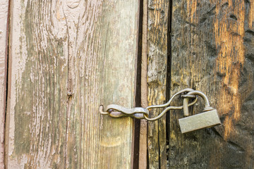 vintage metal lock hanging on an old wooden door with peeling paint outdoors in rural areas