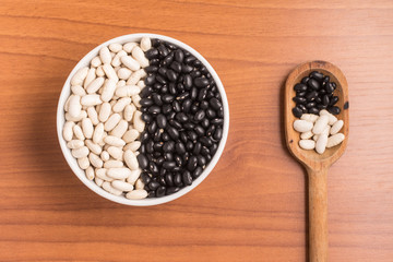 White and black beans into a bowl and spoon over a wooden ta