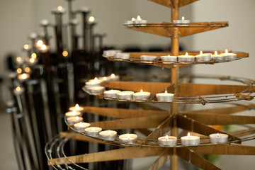 Fototapeta na wymiar Little candles stand on the tired steel holder in the church