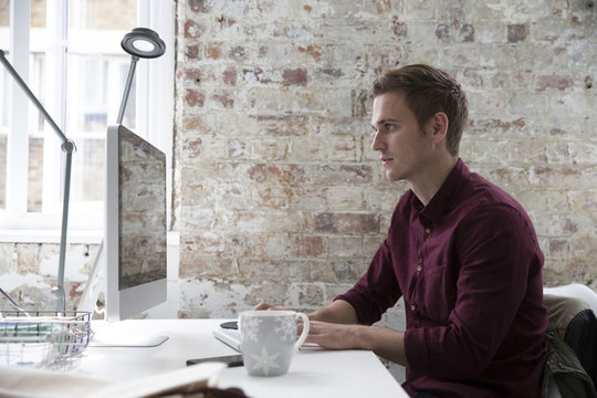 Man In Design Office Sitting At Desk Using Computer