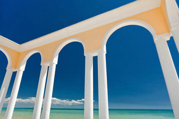Fototapeta na wymiar Rotunda with white columns on the embankment near the blue sea