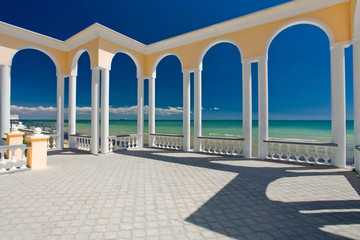 Rotunda with white columns on the embankment near the blue sea