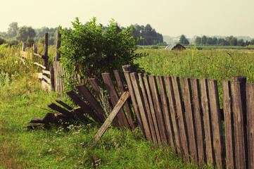 Old broken fence against the field in a summer sunny day