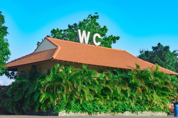 toilet building surrounded by palm trees. on the roof of the large letters WC