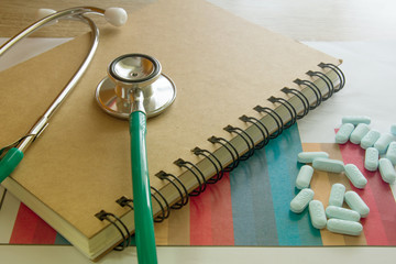A medical stethoscope and pills on paper of graph information and note book , symbol for health care costs or medical insurance ,medical purchasing concept 