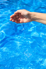 Hand of a girl taking water in the pool in summer. The water drips into the pool.