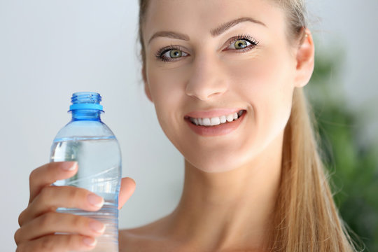 Beautiful girl drinking water on light background
