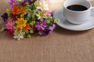 Cup of coffee on sackcloth floor with flowers and vintage sun li