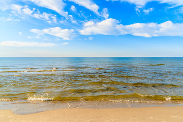 Sea waves on sandy beach and white sunny clouds on blue sky in Debki village, Baltic Sea, Poland