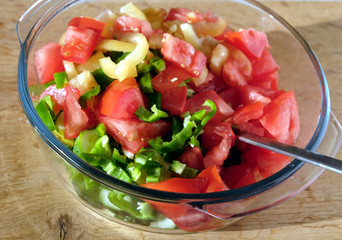 Vegetarian salad from sliced fresh vegetables in round transparent bowl on brown wooden table closeup front view