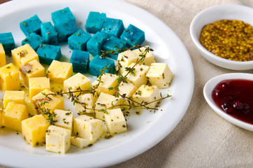 Cheese platter, Gouda, feta, blue pesto cheeses on white plate with herbs, olive oil, pomegranate and mustard sauces