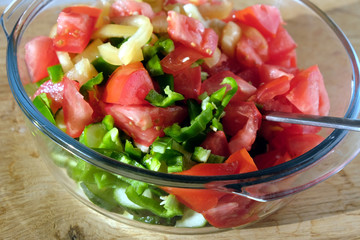 Vegetarian salad from sliced fresh vegetables in round transparent bowl on brown wooden table closeup front view