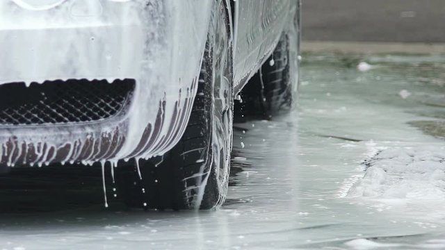 Foamy auto being sprinkled with clear water at wash station, car service center