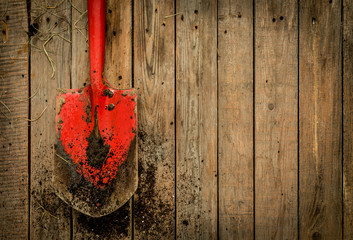 Dirty red spade (gardening tool) on rustic wooden background
