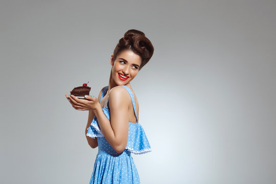 Picture of beautiful pin-up girl holding cake in hands at studio