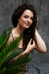 Young beautiful brunette girl in tropical plants over grey background.