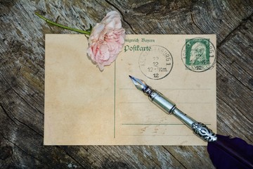alte leere Vintage Postkarte mit alter Briefmarke liegt auf altem Holz mit Rose und Schreibfeder
