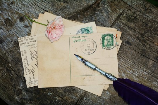 alte leere Vintage Postkarte mit alter Briefmarke liegt auf altem Holz mit Rose und Schreibfeder