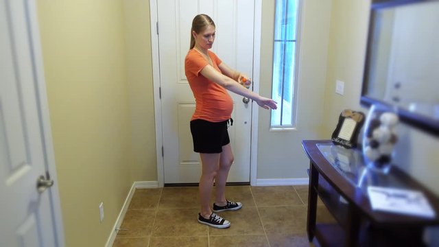 A young pregnant woman stands in her home and uses bug spray on herself before heading outside.	