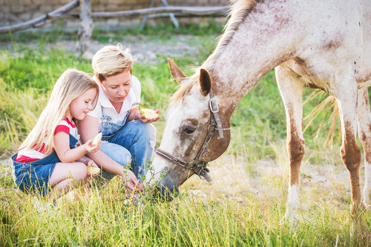 Mother and daughter feeding a horse an apple in the stud.