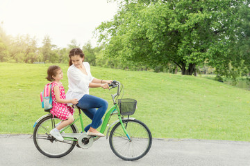 Asian mother and daughter cycling bicycle in park at school. Mot