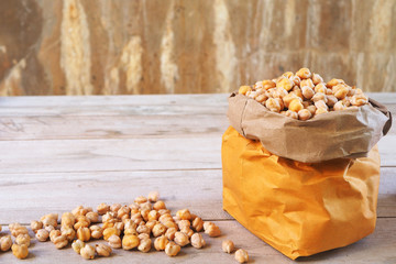 Dried chickpeas in a brown bag and a pile on wooden table.