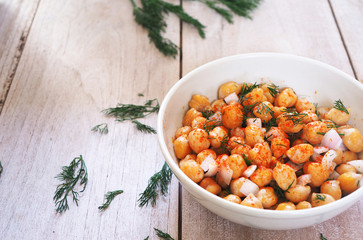 Close up of chickpeas salad in a white bowl on a wooden background.