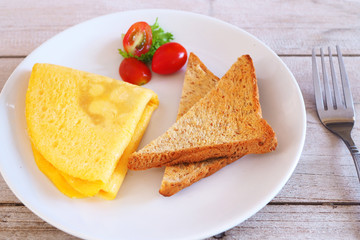 Close up of breakfast with omelette, tomatoes and and toast on a wooden table.