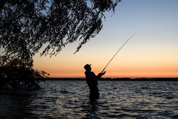Fisherman silhouette at sunset on the lake while fishing   © river34