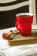 Red cup of coffee on the books, dry flower on a white chair