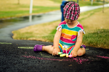 Little girl drawing on pavement with colored chalk