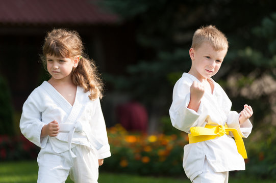 Karate kids in white kimonos, girl and boy, practicing outdoors