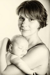 Young woman with newborn baby girl on her hands with smile on her face.