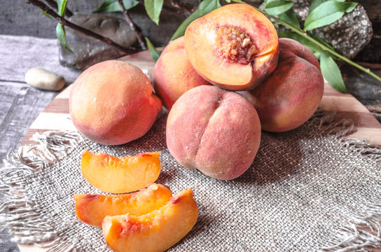 Peaches with slices on a cutting board covered sackcloth on the background of wooden boards
