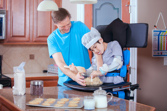 Father helping disabled son bake cookies in kitchen