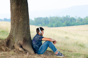 Teenager man sit near tree listen music in headphones